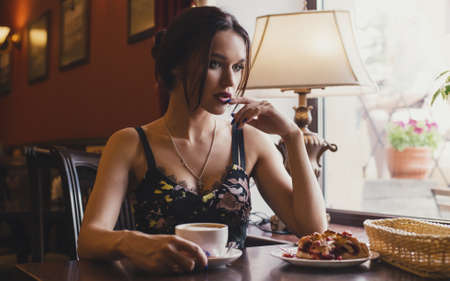 Pensive sexy girl in sitting at the cafe going and drinking coffee with dessertの写真素材