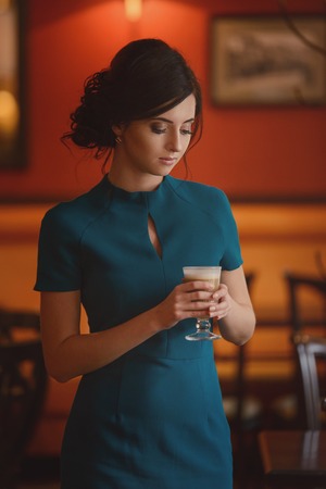 Pensive pretty girl in classic elegant dress standing at the cafe going to drink coffeeの写真素材