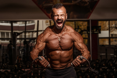 Handsome man with big muscles working out in gym. Muscular bodybuilder doing exercises
