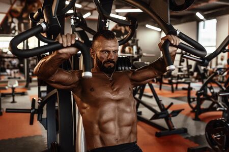 Handsome man with big muscles working out in gym. Muscular bodybuilder doing exercises
