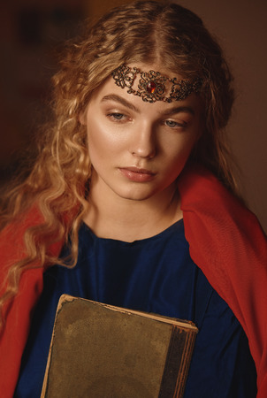 Retro portrait of a beautiful dreamy young woman holding a book in hands outdoors. Soft vintage toningの写真素材