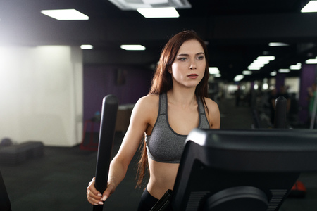 Attractive fitness girl doing exercise on machine treadmill. Pretty girl doing workout at modern...