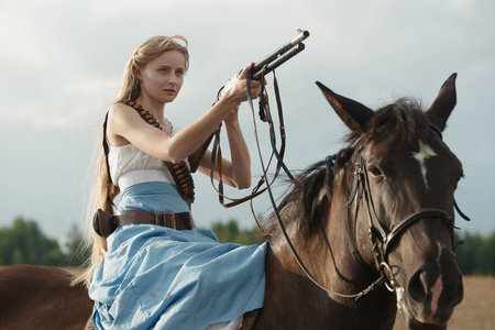 Portrait of a beautiful female cowgirl with shotgun from wild west riding a horse in the outback