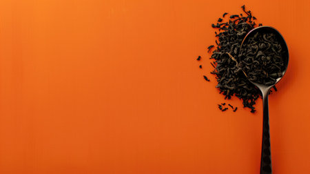 Black tea leaves spilling from spoon on orange backgroundの素材