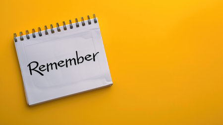 Spiral notebook with word "Remember" written on page against yellow backgroundの素材