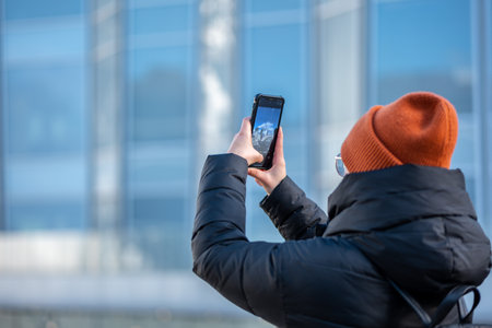 Young man in winter jacket and hat with mobile phone in the city