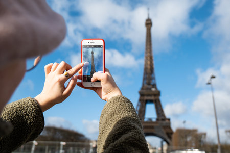 Woman taking photo of Eiffel tower in Paris, France using smartphoneの写真素材