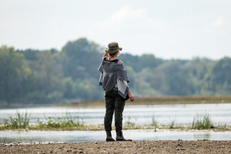 A woman in a hat stands on the bank of a lakeの写真素材