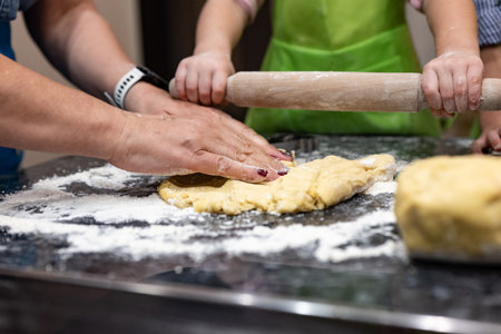 Close up of female hands kneading dough with rolling pin in kitchen