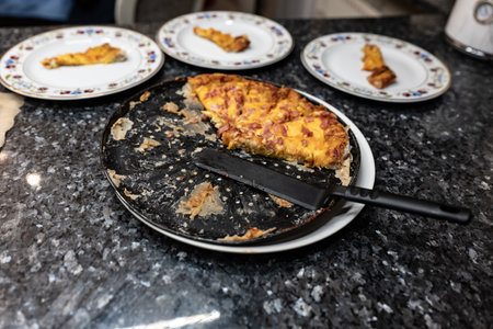 Piece of pizza with bacon and cheese on a black plate.の写真素材