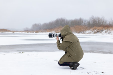 Photographer with a camera on the bank of a frozen river.の写真素材