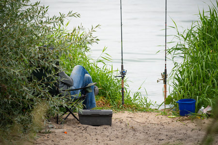 Fisherman sitting on the shore of the lake with fishing rodの写真素材