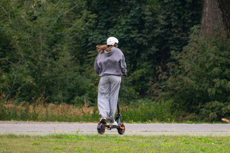 A young woman riding an electric scooter on a country road.の写真素材
