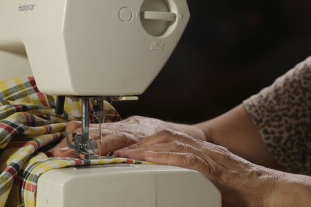 Home Sewing. Elderly woman working at the electro-mechanical sewing machine.