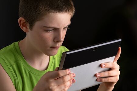 Teenage Pastime. Teenage boy holding tablet computer, looking at computer screen, on black background.の写真素材