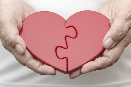 Two Halves of One Heart. Erderly woman holding jigsaw puzzle in shape of heart. Photography snapshot on the subject of 'Gender Relations'.の写真素材