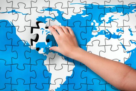The Final Piece. Child's hand, inserting missing piece of jigsaw puzzle into the map empty place. Photomontage, combined from photography and 3D-rendered image.の写真素材