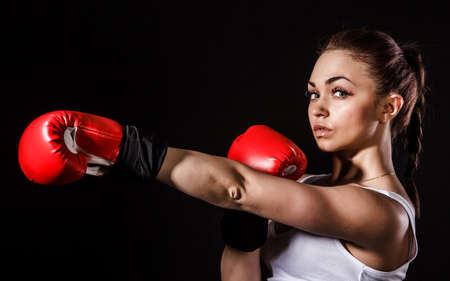 Beautiful young woman in a red boxing gloves over black backgroundの写真素材