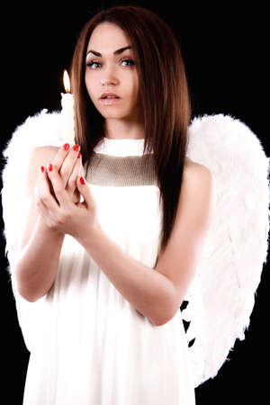 Beautiful young angel holding a candle over black backgroundの写真素材