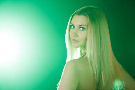 Beautiful young woman looks around at the backround of the bright green lightの写真素材