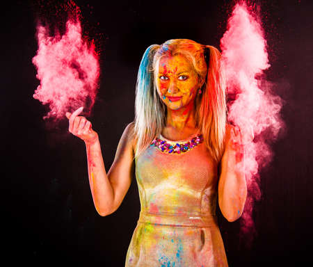 Beautiful young woman covered with colored powder over dark background