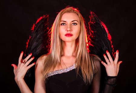 Beautiful young woman with black angel wings over dark red backgroundの写真素材