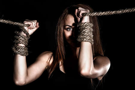 Beautiful young woman with tied arms over black backgroundの写真素材