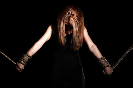 Beautiful young woman with tied arms over black backgroundの写真素材