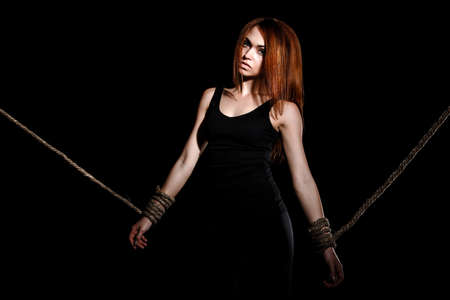 Beautiful young woman with tied arms over black backgroundの写真素材