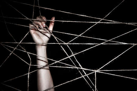 Slim hand behind the interlaced ropes over black backgroundの写真素材