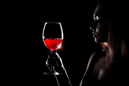 Beautiful young woman holding the glass of a red wine in darknessの写真素材