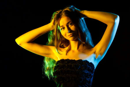 Beautiful young woman in yellow lights over black backgroundの写真素材