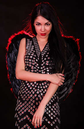 Beautiful young woman with black angel wings over dark red backgroundの写真素材