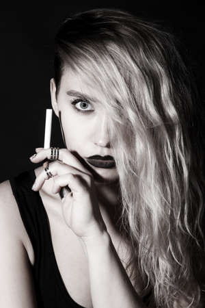Beautiful young woman smoking a cigarette over black backgroundの写真素材