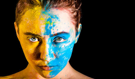Beautiful young woman covered with yellow and blue paintsの写真素材