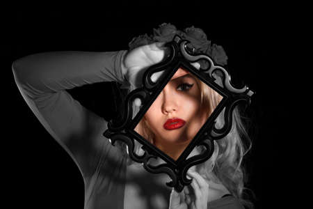 Pretty young woman holding a frame in front of her face over black background