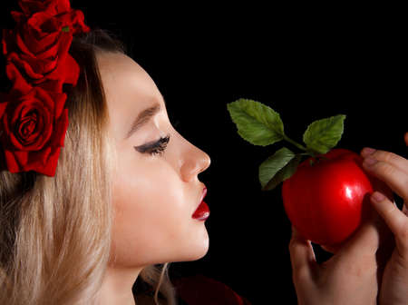 Closeup portrait of a young lady holding a red apple over black backgroundの写真素材