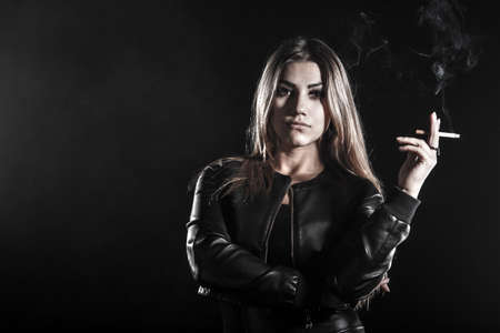 Beautiful young woman smoking a cigarette over black backgroundの写真素材