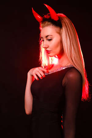 Beautiful young woman with red demon horns over black background