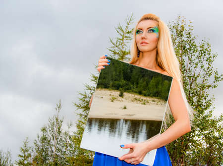 Beautiful young woman holding mirror at the countrysideの写真素材