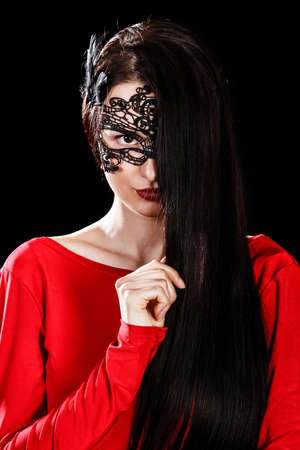 Beautiful young woman sitting in a black mask over black backgroundの写真素材