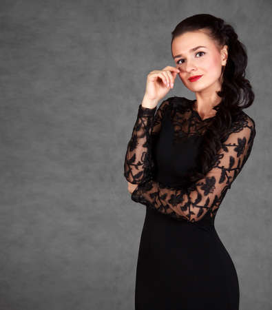 Portrait of a young attractive woman in a black evening dress over grey backgroundの写真素材
