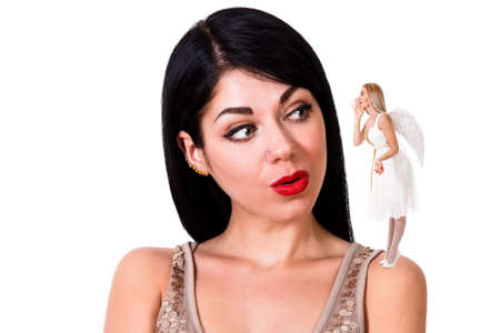 Beautiful young woman listening to the angel staying on her shoulder isolated over white backgroundの写真素材