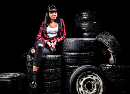Young woman in a red checked shirt sitting on a tires over black backgroundの写真素材