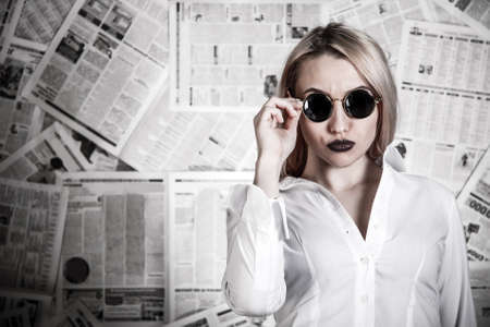 Young blonde in a sunglasses surrounded with newspapersの写真素材