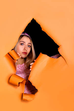 Pretty young woman looking through a hole in an orange paper