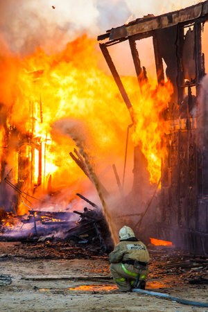Fireman extinguishes a burning old wooden residential houseのeditorial素材