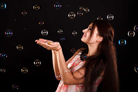 Beautiful young woman playing with soap bubbles over black background