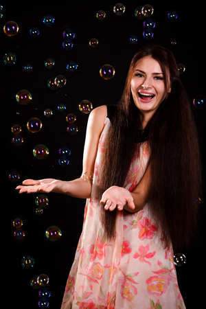 Beautiful young woman playing with soap bubbles over black backgroundの写真素材