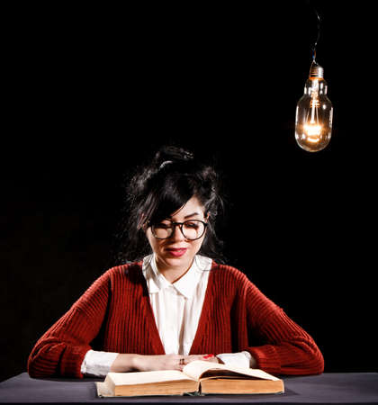 Pretty young woman reading under the light bulb